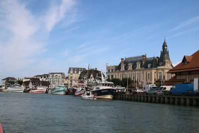 Boats moored in canal by buildings against sky on sunny day