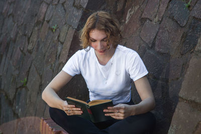 Young woman sitting on book against wall