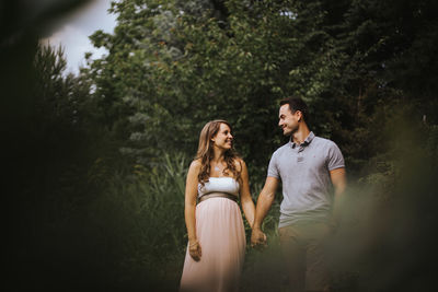 Husband with pregnant wife holding hands in forest