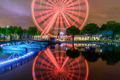Reflection of illuminated ferris wheel in lake against sky at night