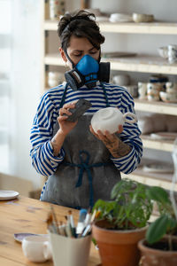 Professional pottery artisan polishes the finished product in a respirator