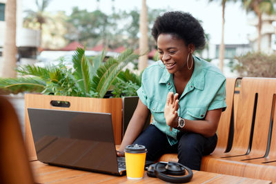 Cheerful young woman using laptop on table at outdoor cafe