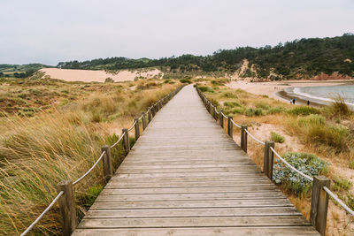 Rear view of man walking on boardwalk against sky