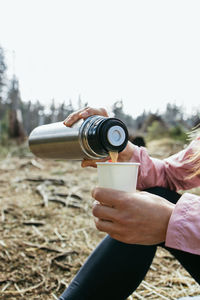 Close-up of a woman's hands pouring coffee from a thermos in the forest. rest at nature. hiking
