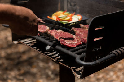 Cropped image of hand preparing meat on barbecue grill
