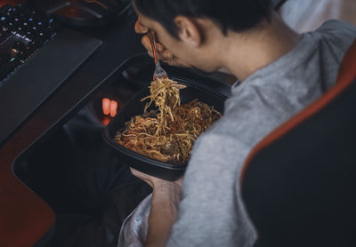 Young caucasian guy gamer eats wok food with a fork from a black container