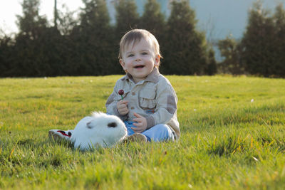 Portrait of cute, smiling baby boy with a white fluffy bunny on field