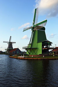 Traditional windmill by river against sky