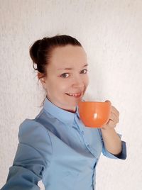 Portrait of smiling woman holding ice cream against wall