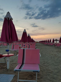 Chairs on beach against sky during sunset