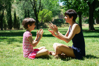 Side view of mother playing with daughter on grassy land in park