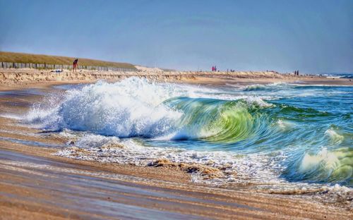 Waves splashing on shore against clear sky