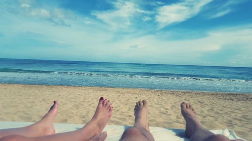 Low section of people at beach against sky