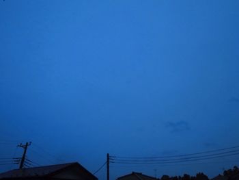 Low angle view of silhouette electricity pylon against blue sky