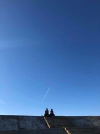 Low angle view of people standing against clear blue sky