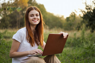 Portrait of young woman using laptop while sitting on field