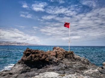 Flag on rock by sea against sky