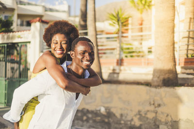 Boyfriend piggybacking girlfriend in city during sunny day