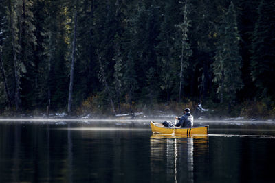 People sitting on lake against trees in forest