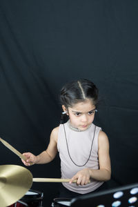 Girl playing drum while standing against curtain