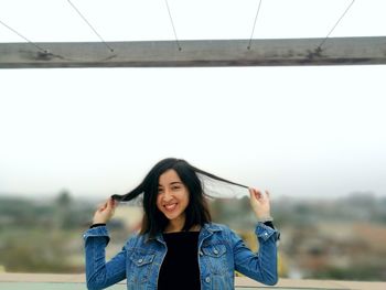 Portrait of a smiling young woman standing against sky
