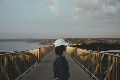 Side view of woman standing on footbridge against sky