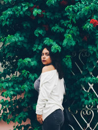 Portrait of beautiful young woman standing against trees