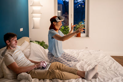 Side view of woman using mobile phone while sitting on bed at home