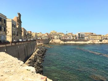 View of buildings by sea against clear blue sky