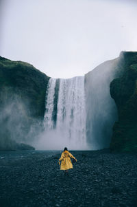 Rear view of man looking at waterfall against sky