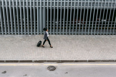 High angle view of woman with luggage walking on footpath in city