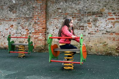 Side view of girl playing on spring ride against old wall