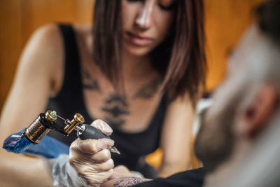 Female tattoo artist tattooing mans arm in studio