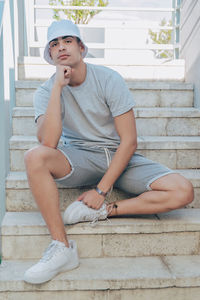 Full length of young man sitting on staircase against wall