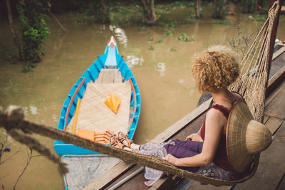 Side view of mid adult woman with hat sitting on hammock over lake