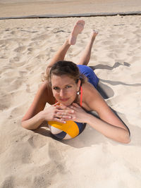 Portrait of woman lying with volleyball on sand at beach