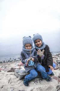 Girl in knitted grey hat sharing gloves with her frozen brother