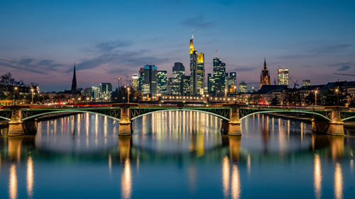 Illuminated bridge over river in city against sky at night