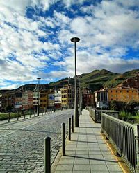 Footpath leading towards building against cloudy sky