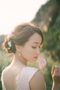 Rear view of mid adult woman with eyes closed holding flower while standing against sky