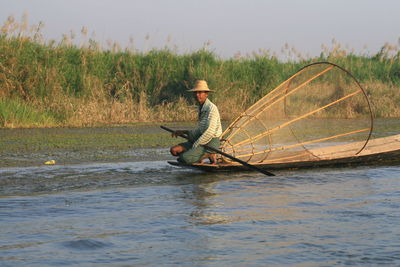 Side view of fisherman crouching on fishing boat in river