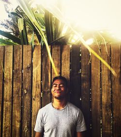 Portrait of young man standing against wooden fence