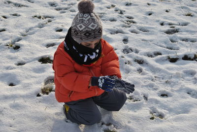 Boy crouching on snow covered field
