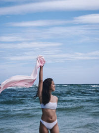 Rear view of woman with arms raised in sea against sky