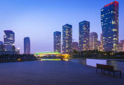 Illuminated buildings in city against clear sky at dusk