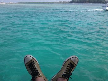 Low section of man with canvas shoes over sea