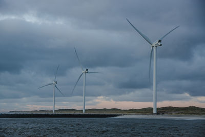 Windmills by sea against sky