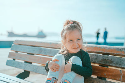 Smiling girl sitting on bench looking away