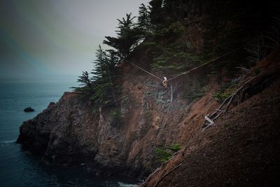 Woman practicing slacklining on cliff by sea