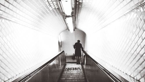Rear view of woman walking on escalator in tunnel